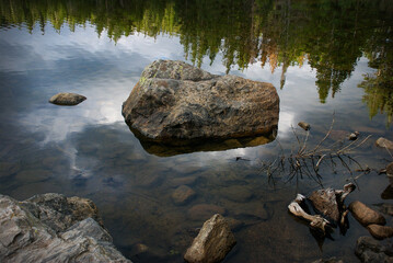 Fototapeta na wymiar Boulder in Bear Lake, Rocky Mountain National Park, Colorado USA with pine forest and cloudy sky reflected in water.