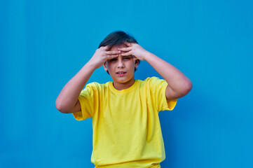 Portrait of boy with worried face in yellow t-shirt, on blue background. Copy space