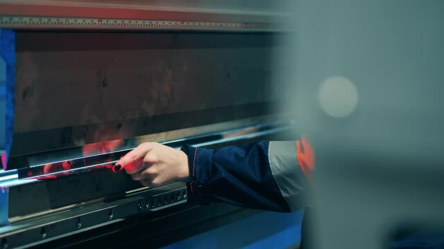 Factory worker manually bending a metal plate using a machine