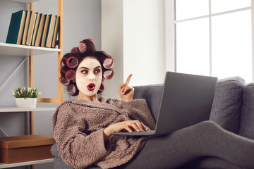 Surprised woman points finger up as she finds amazing idea online. Happy lady in curlers and face...