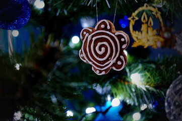 Decorated gingerbread in the shape of flower hanging on the glowing Christmas tree; beautiful Christmas decoration