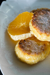 Delicious cottage cheese pancakes with powdered sugar, with an orange on a white plate close-up. Vertical photo