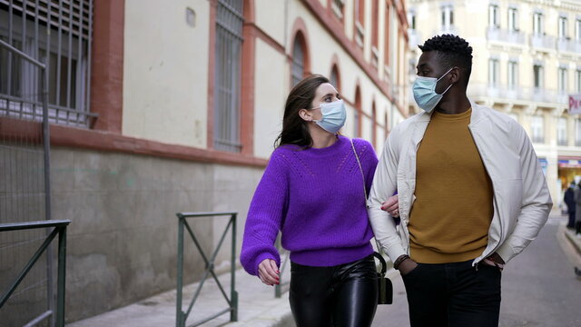 Interracial diverse couple wearing covid-19 face masks walking outside in street.