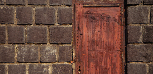red metal door and a fragment of a gray stone wall, rust under the paint, wall masonry from old stone blocks, background texture of an ancient brick wall