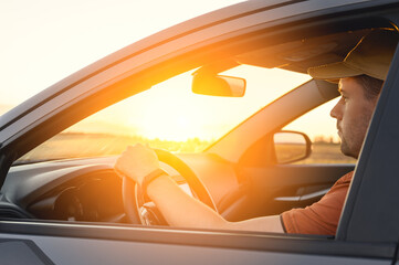 Caucasian Man in automobile in the countryside and sun rays. Male driver driving a car at sunset background. Summer travel, road trip and vacations concept
