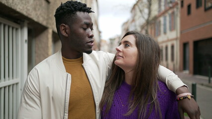 Interracial young couple walking together in city street. Black man arm around girlfriend