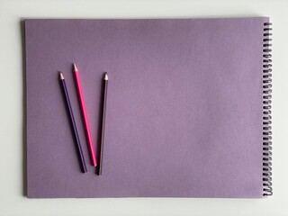 Colored pencils on purple paper album on white table. Artist, art and hobby. Drawing and painting
