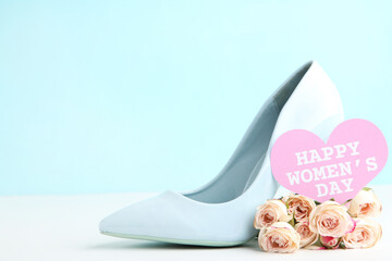Rose flowers and card in shape of heart with text Happy Womens Day and high-heeled shoe on blue background