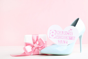 Card in shape of heart with text 8 March Womens Day, gift box and blue high-heeled shoe on pink background