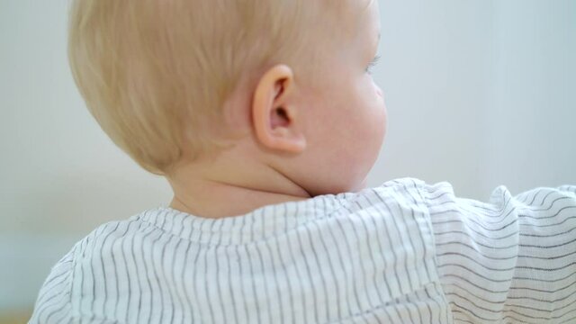 Baby boy with blonde hair wearing striped shirt crawling on floor and playing with toy. Closeup little child from behind having fun at home. Concept of babyhood