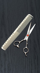 Beautiful hairdressing scissors with a red stone and a comb, lie on a black table.