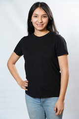 Young Woman Black T-Shirt Mockup - Black Shirt Template, Front View - Portrait of Young Hispanic Woman Smiling with Hand on Waist on White Background