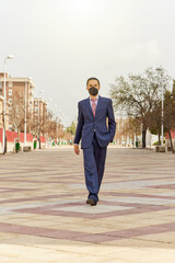 Businessman outdoors talking on the phone in front of a white building with ffp2 mask. Young entrepreneur guy working abroad.