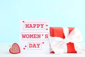 Fototapeta na wymiar Card with text Happy Womens Day, gift box and heart in shape of clothespin on blue background