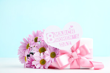 Chrysanthemum flowers, gift box and card in shape of heart with text 8 March Womens Day on blue background