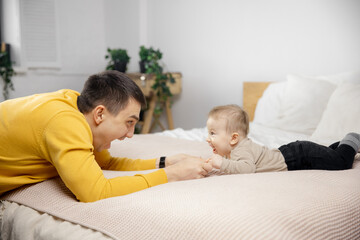 Young father is playing with newborn baby on bed