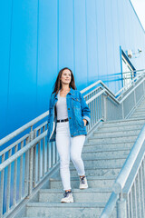 Lifestyle portrait of a beautiful and happy young woman walking down stairs in the street with blue background
