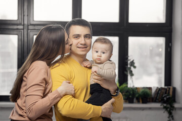Happy parents are smiling with small baby son on background of window