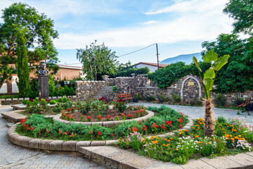 Flowerbeds and decorative stone buildings in city public garden. In background there is bust of Girey Bairov. Shot in Alushta, Crimea