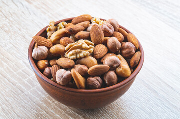 a mixture of nuts in a clay plate on a wooden table, a concept of healthy food, top view