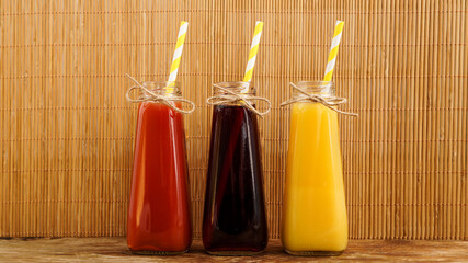 Three multicolored drinks in the bottles on a wooden bamboo background. Bottled paper straws. Full...