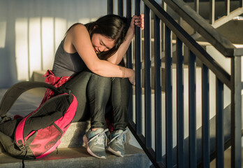 young depressed and scared Asian Japanese student girl suffering abuse and harassment at school victim of bullying and discrimination sitting on college staircase tormented