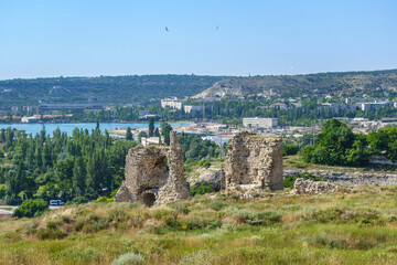 Fototapeta na wymiar Panorama of medieval towers of Kalamita, fortress founded by Byzantines. It was built above cliff hiding cave church of St Clement. Modern city Inkerman (Crimea) and Sevastopol bay are on background
