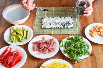 young woman prepares sushi with fresh ingredients at home. on wooden table.