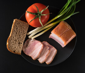 Food, Sliced bacon, tomato green onion and a piece of black bread, on a black plate on a black background