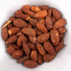 Top view of a pile of salted roasted almonds in a white round bowl