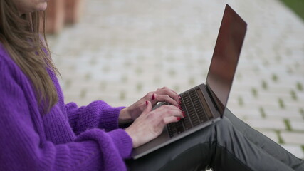 Young woman working remotely in front of her laptop computer outside