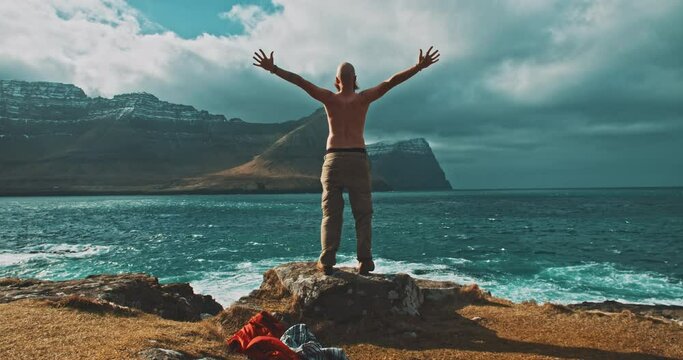 Topless man in front of the ocean with open arms. 
