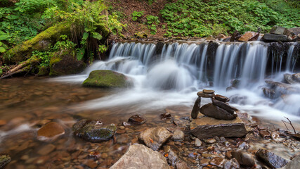 Obraz premium Stacked stones on mountain river beside the waterfall