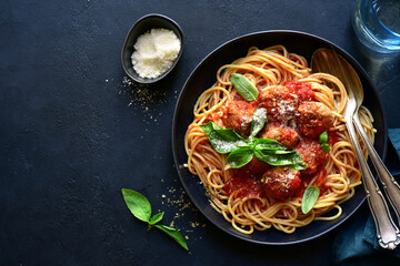 Spaghetti with meat balls in tomato sauce in a black bowl. Top view with copy space.