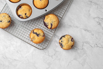 Blueberry Muffins in a Silver Muffin Tin on Wire Rack on a White and Gray Marble Countertop