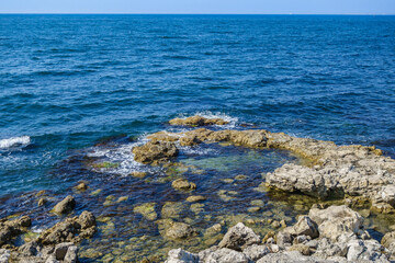 Sea waves washing shore stones. Calm water, clear sky and small silhouette of ship on far horizon