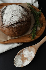 Freshly baked flour bread on a dark background and rosemary. The round bread lies on a wooden plate.