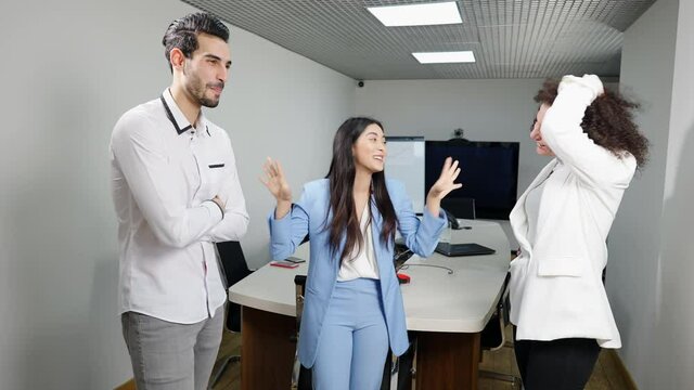 Portrait of excited Asian woman talking with positive multiethnic colleagues standing in office. Happy smiling beautiful employee telling story to Middle Eastern man and Caucasian woman indoors.