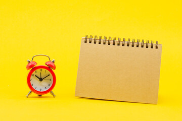 red round analog alarm clock isolated on yellow background. time 10:10. craft notebook. space for text.