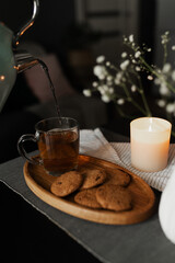 A woman pours tea into a mug from a teapot. Tea and cookies on the kitchen table.