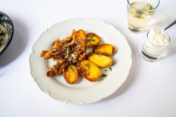 Fried sardines with potato on white plate, garlic yogurt in glass, wine and part of pan