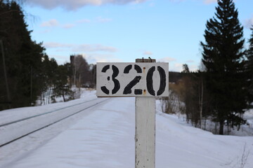 320 km of rail road sign in winter day with forest trees in snow and cloudy blue sky