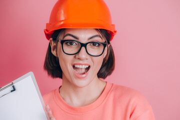 Smiling woman worker builder hold white sign board blank against pink background. Building helmet.