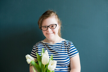 Portrait of teenage girl with Down syndrome standing with flowers on blue background. Disability children. World Down syndrome day.