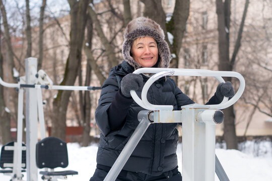 Old woman is engaged in sports on the gym equipment in the park.