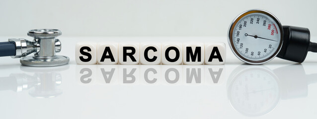 On a reflective white surface lies a stethoscope and cubes with the inscription - SARCOMA