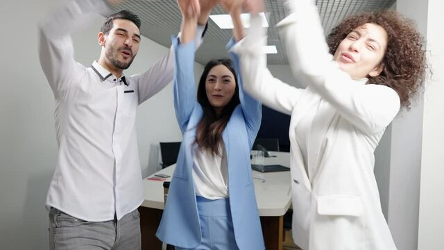 Positive laughing young millennial multiracial coworkers stacking hands in office. Happy cheerful Caucasian, Asian and Middle Eastern colleagues rejoicing success indoors. Business lifestyle.