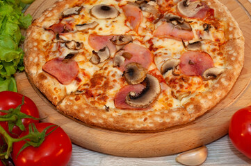 Pizza with ham, mushrooms and cheese on a board with tomatoes and green salad