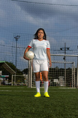 Latin female soccer player standing with the ball in the soccer field. Female football player © Julian