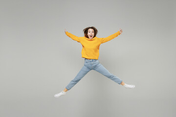 Fototapeta na wymiar Full length of young excited overjoyed expressive woman in knitted yellow sweater in air jump high with outstretched hands legs on workspace mock up isolated on grey color background studio portrait